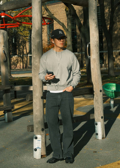 Light grey crewneck sweatshirt for men styled with relaxed black jeans in an outdoor fall setting.