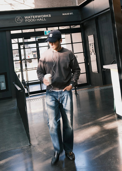 Black crewneck sweatshirt styled casually with blue washed jeans, in an indoor setting. 