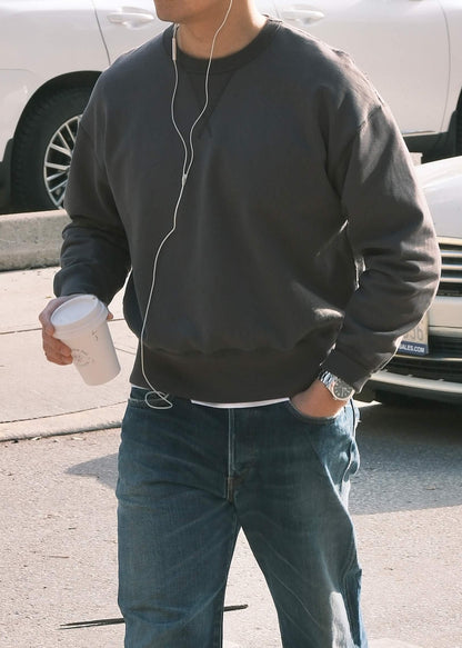 Black crewneck sweatshirt styled casually with blue washed jeans, in an outdoor setting. 