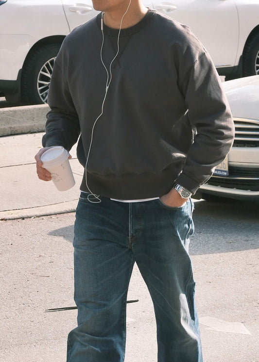 Black crewneck sweatshirt styled casually with blue washed jeans, in an outdoor setting. 
