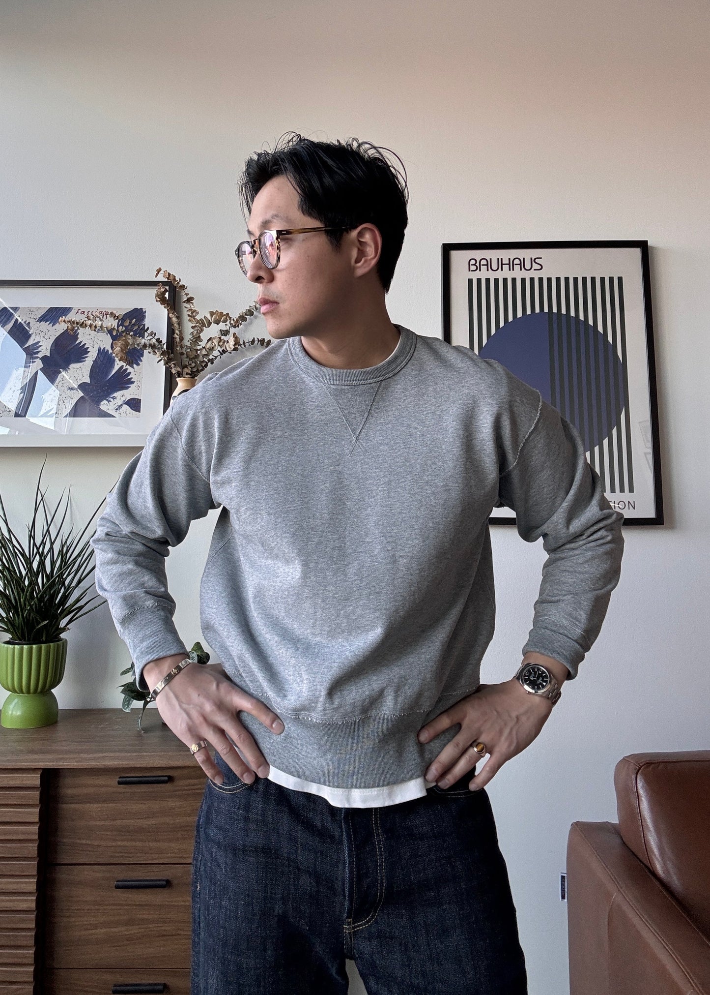 Man wearing a gray sweater and glasses in a room with decor elements.